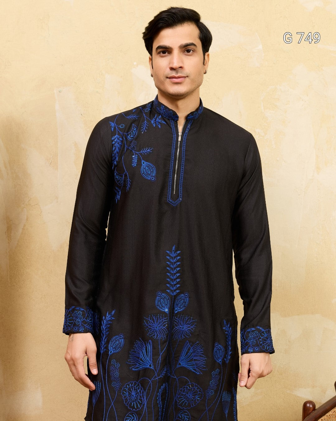 Man wearing a black kurta with blue embroidery against a beige background