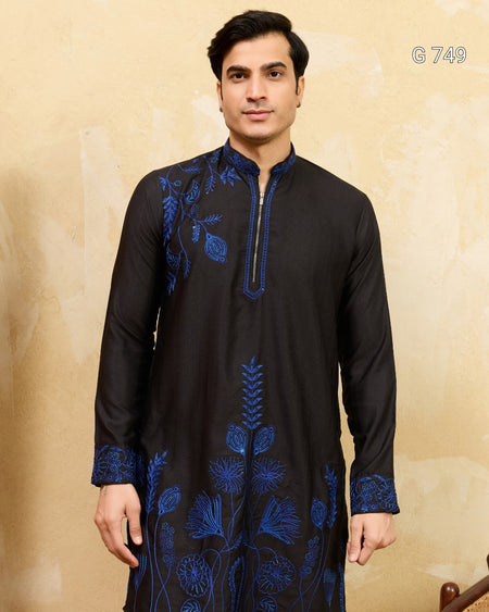 Man wearing a black kurta with blue embroidery against a beige background