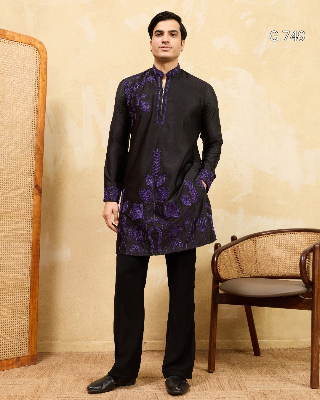 Man wearing a black kurta with purple embroidery against a beige wall.