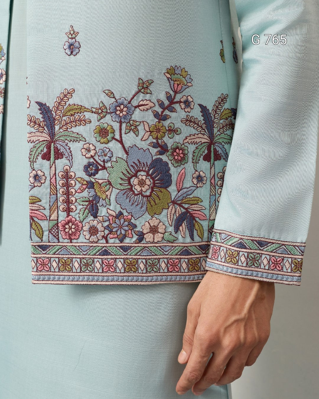 Light blue fabric with intricate floral embroidery and a hand holding it.