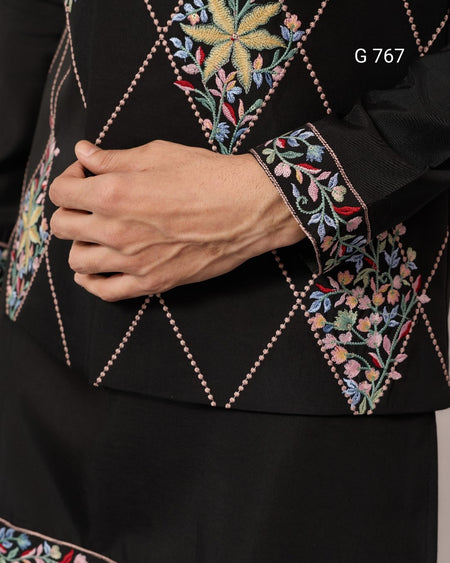 Close-up of a black garment with colorful floral embroidery on a plain background