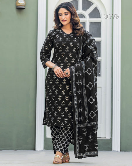 Woman wearing a black patterned outfit with a matching dupatta in front of a white door.