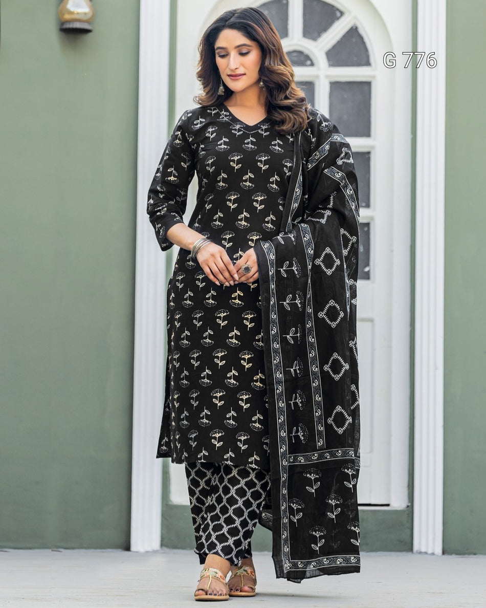 Woman wearing a black patterned outfit with a matching dupatta in front of a white door.