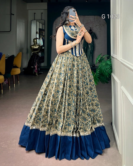 A woman takes a mirror selfie in a boutique wearing a traditional Indian Anarkali gown. The dress features a navy blue velvet border and a beige and green floral print on the skirt, with a matching navy blue and gold embroidered bodice.