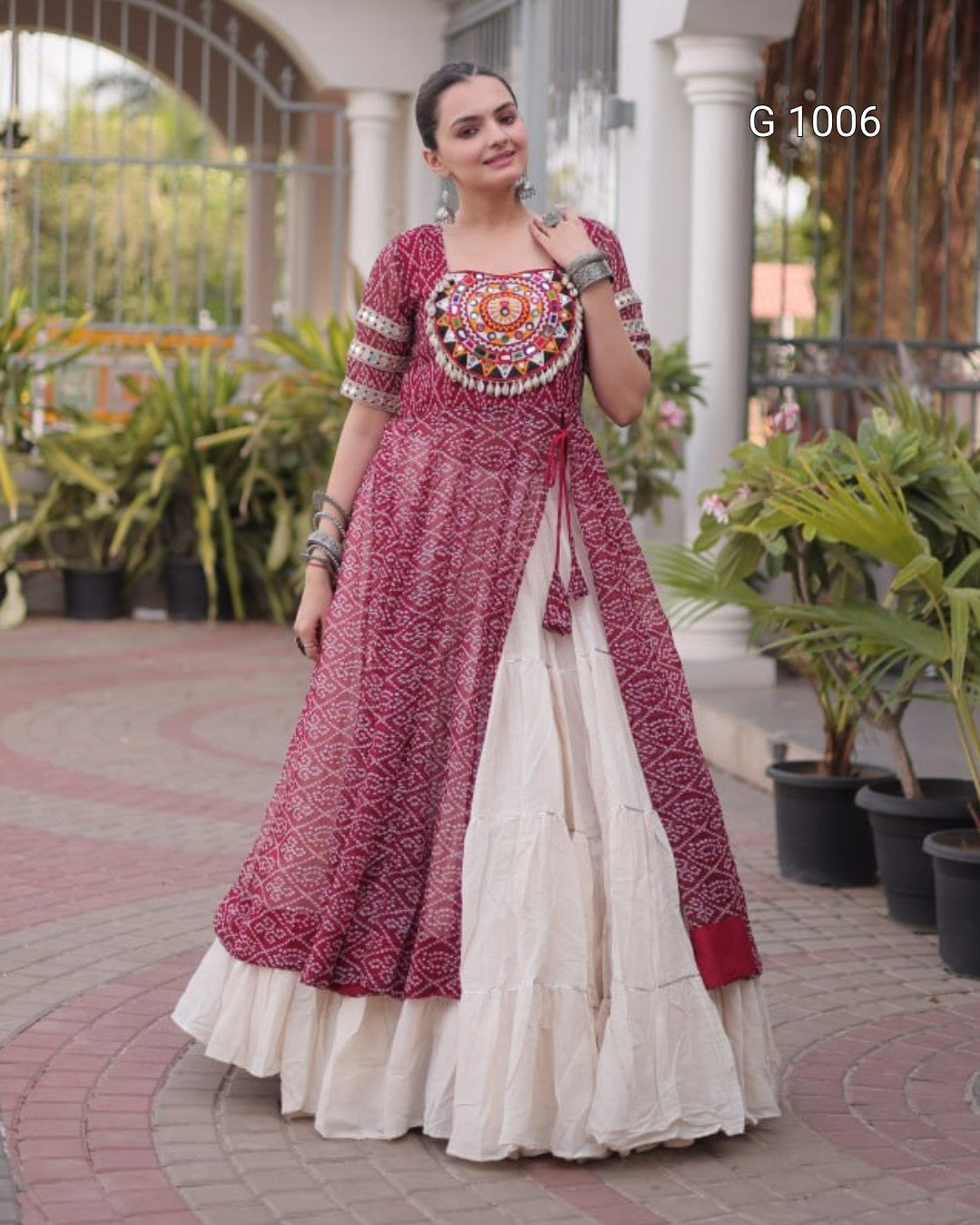 A woman models a traditional Indian salwar kameez outfit with a dusty rose printed kurta and a cream-colored flared skirt, standing in an outdoor courtyard with potted plants.