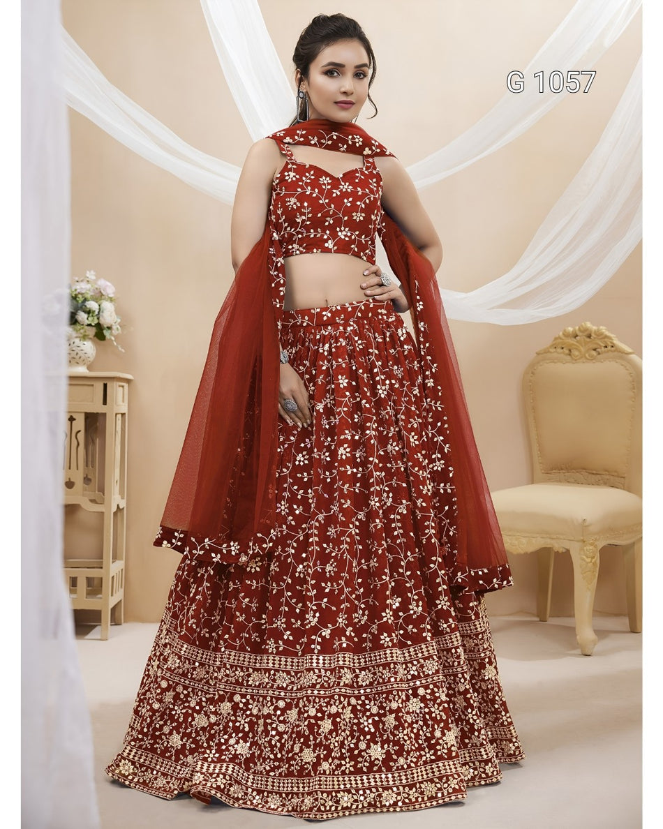 A woman models a traditional Indian red lehenga choli set with intricate gold and white floral embroidery, set against a decorated beige background with draped white fabric.