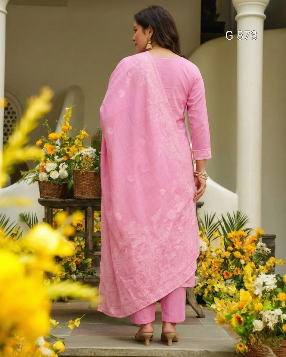Woman in a pink traditional outfit standing in a decorated outdoor setting with flowers and plants.