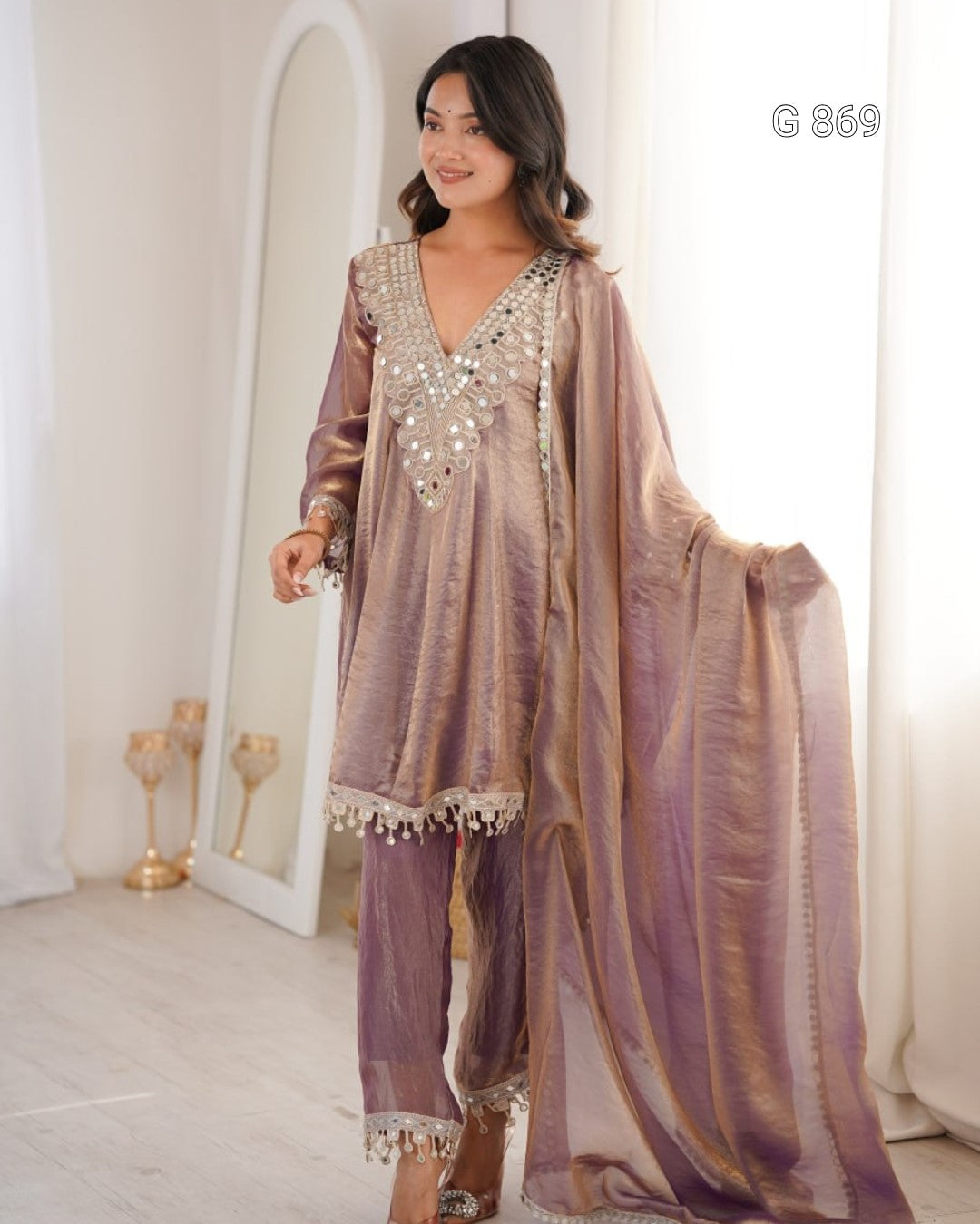 Woman wearing a traditional outfit with intricate designs in a bright room.
