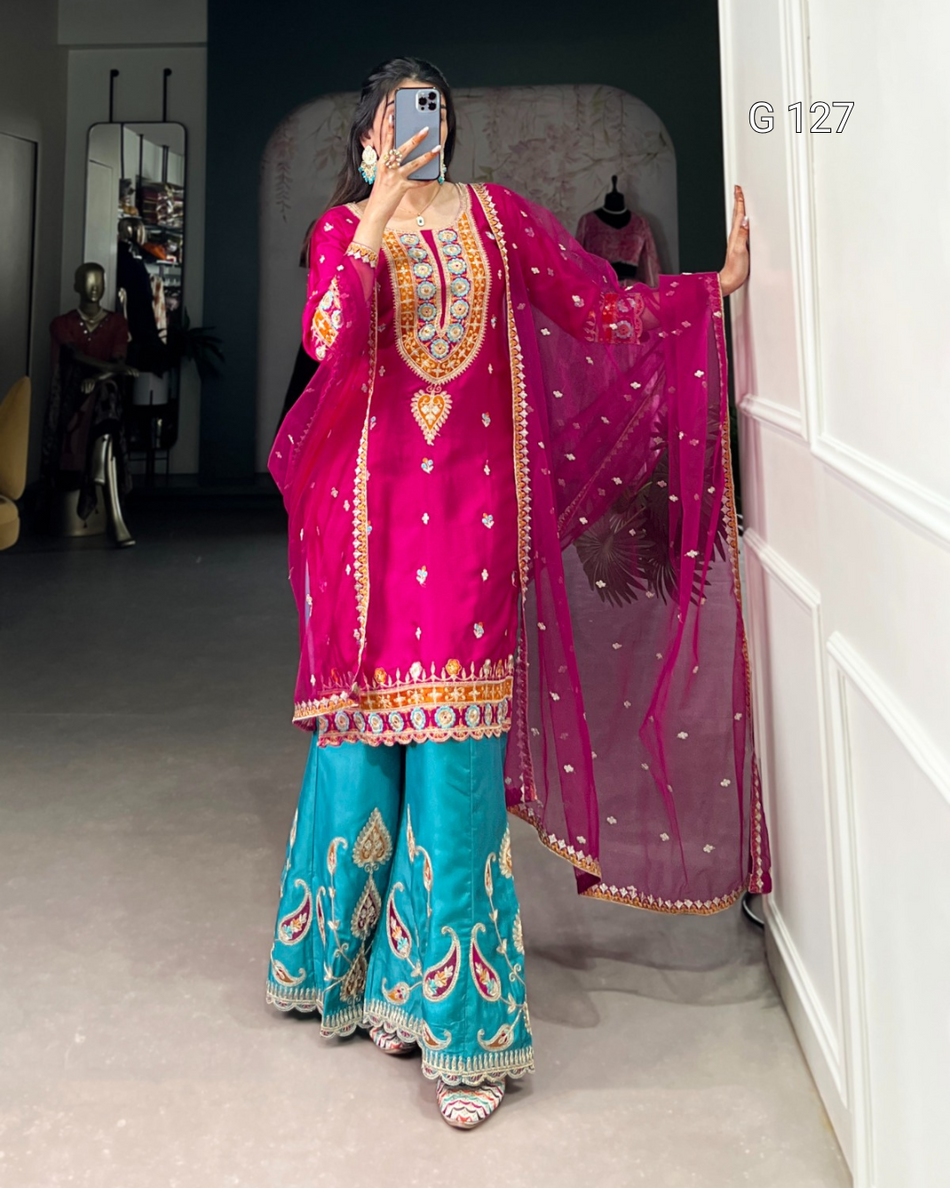 Person wearing a traditional outfit with pink and blue colors, standing in a room.