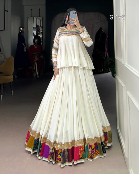 Person wearing a long, white dress with colorful patterns in a room.