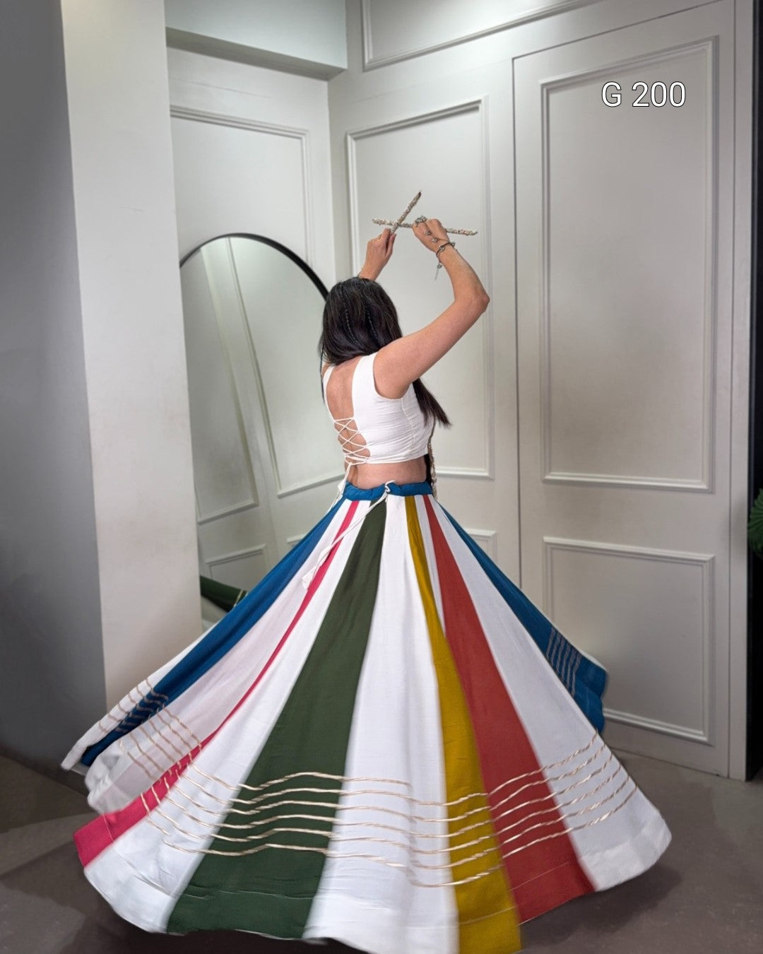 Woman wearing a colorful skirt with a white top, standing in front of a mirror.