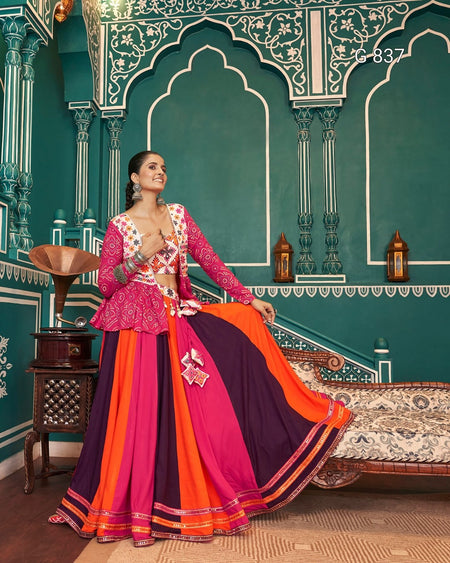 Woman in a colorful traditional outfit standing in a decorated room with green walls and ornate details.