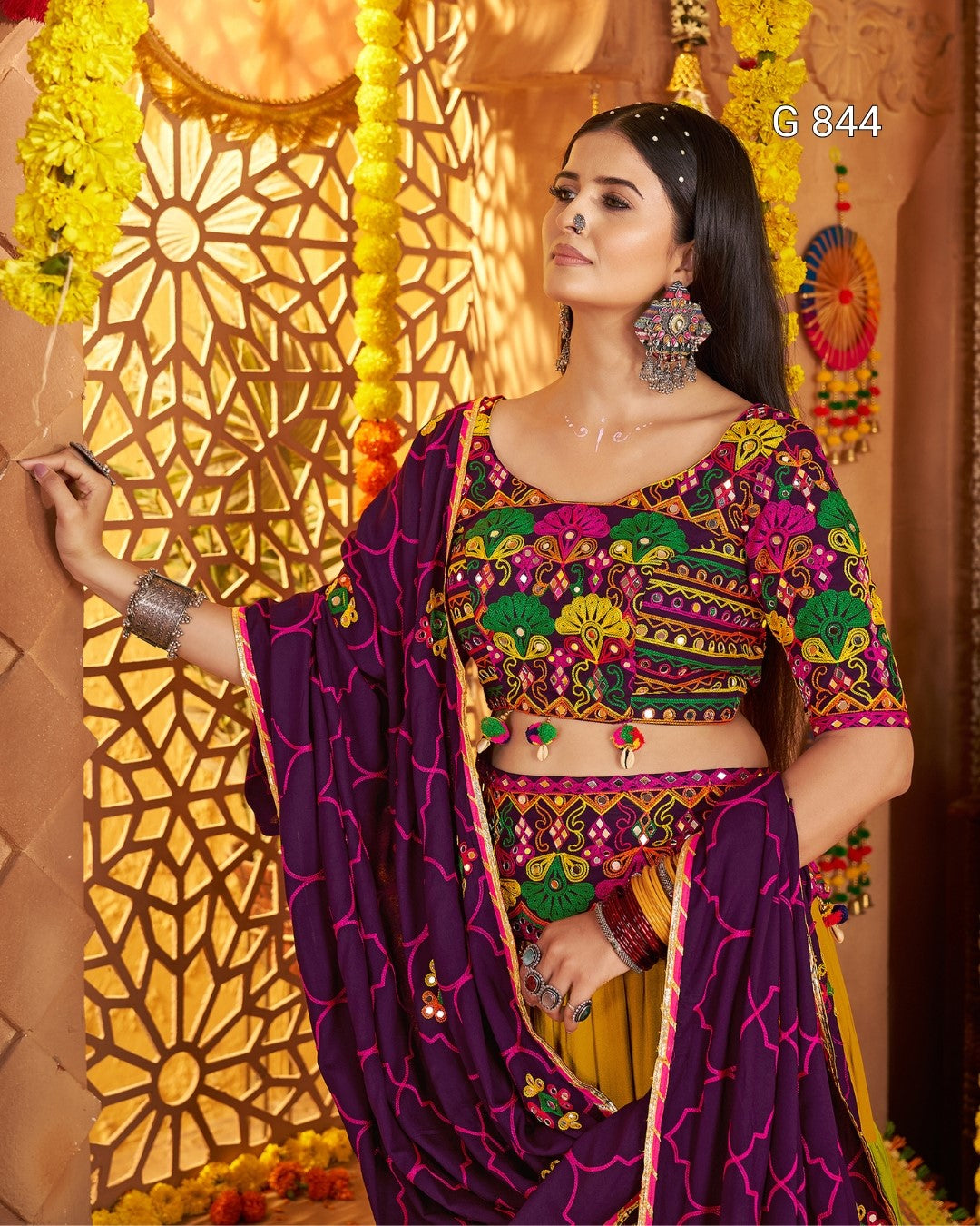 Woman in traditional colorful outfit with intricate patterns, standing against a decorative background.