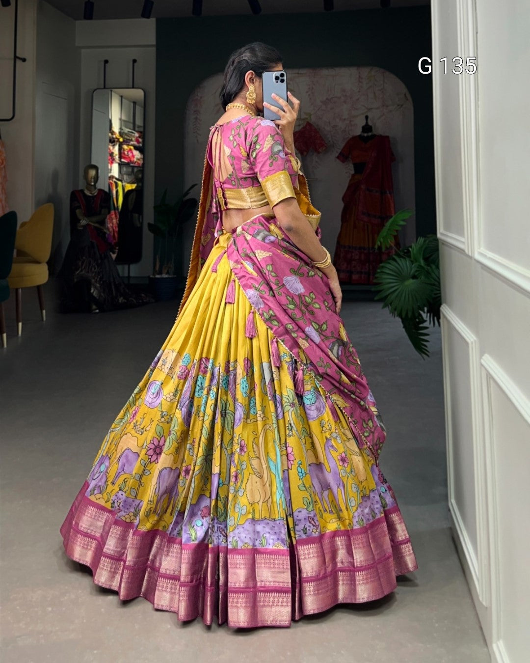 Woman in a yellow and pink saree taking a mirror selfie in a room.