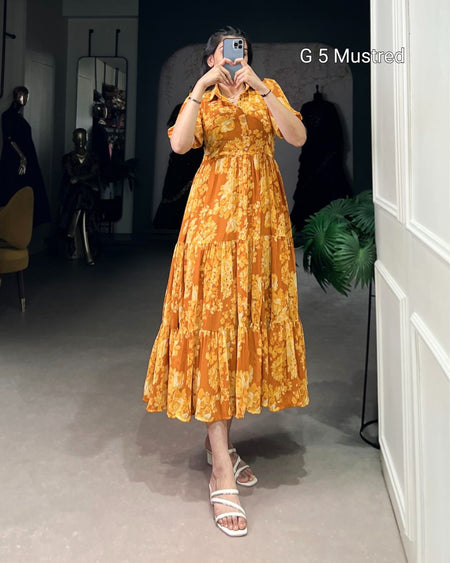 Person wearing a yellow floral dress in a room with a mirror and plant.