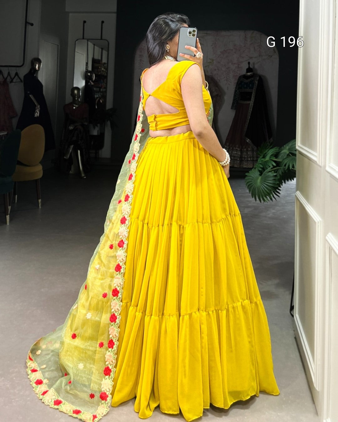 Woman wearing a yellow saree with a floral border in an indoor setting.