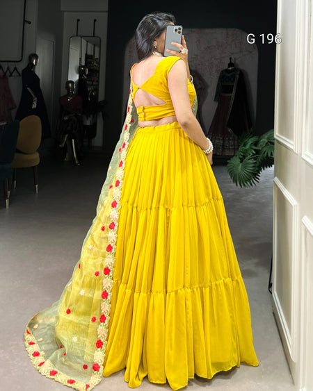 Woman wearing a yellow saree with a floral border in an indoor setting.