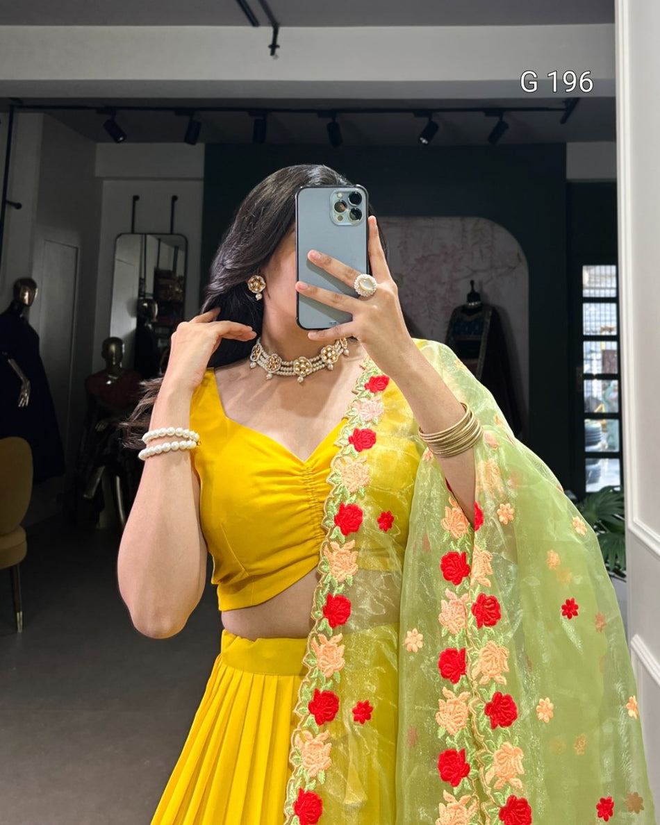 Person wearing a yellow outfit with a green dupatta featuring red and orange floral patterns, taking a mirror selfie.