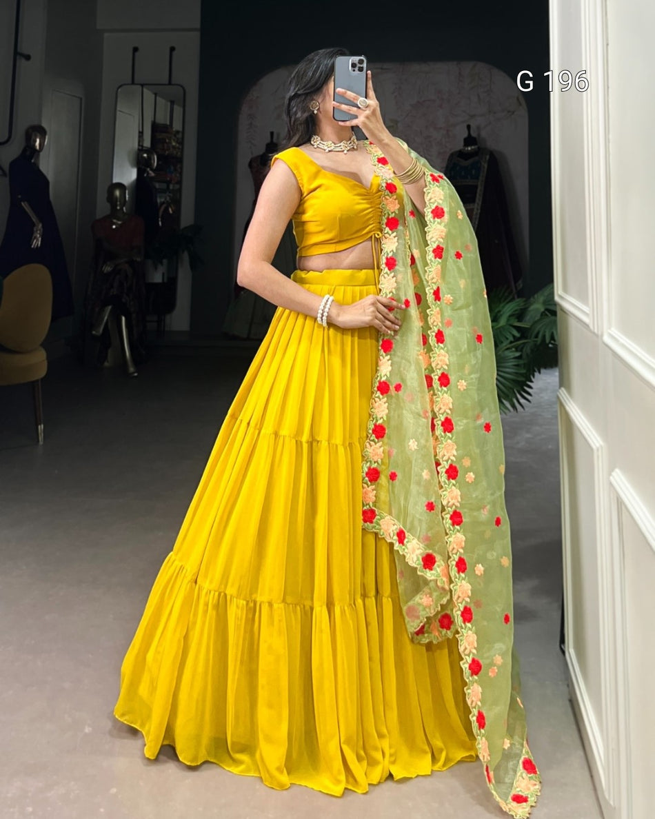 Woman in a yellow traditional outfit with a green dupatta featuring red and gold patterns, taking a mirror selfie.