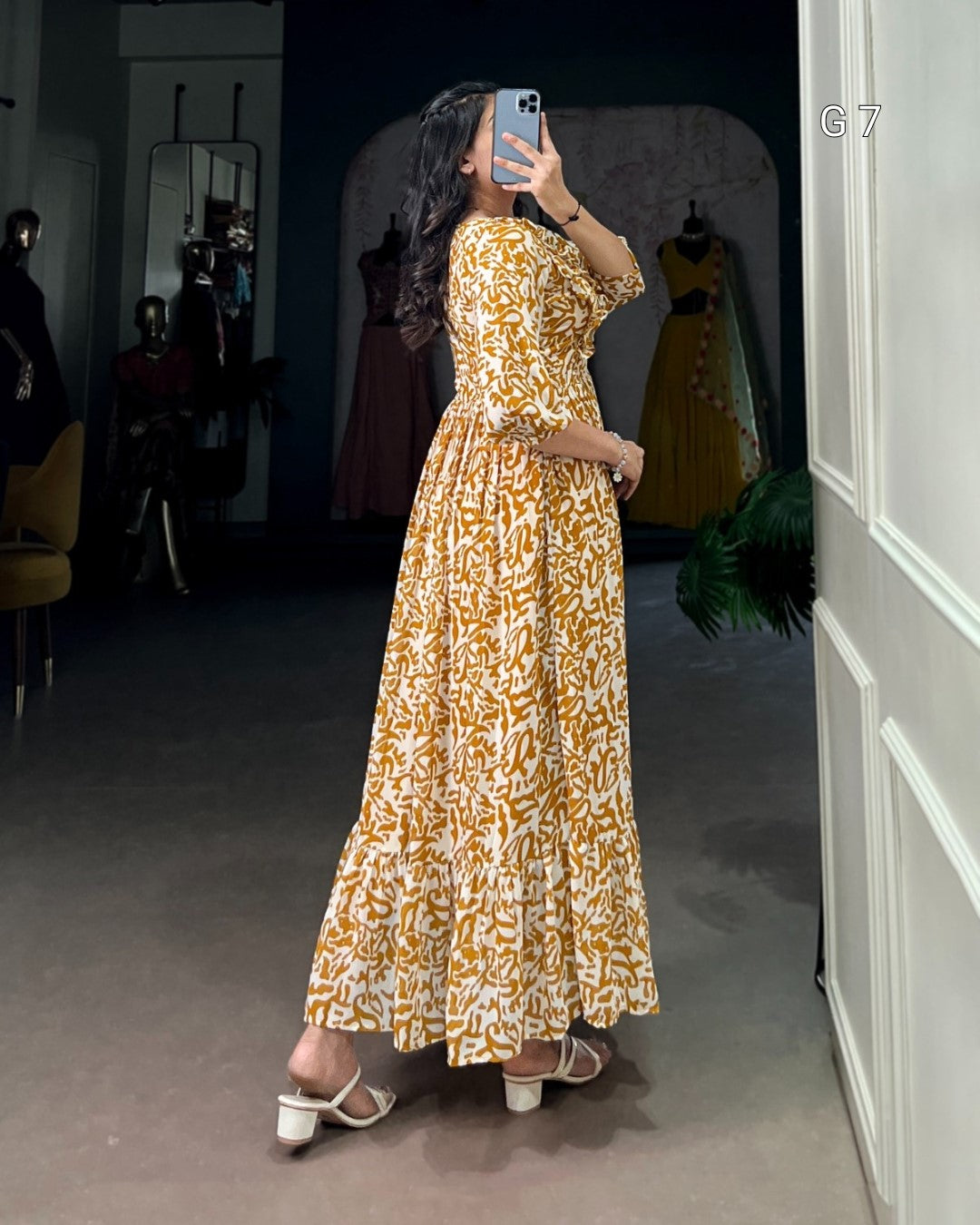 Woman taking a mirror selfie wearing a yellow floral dress in a room with mannequins.