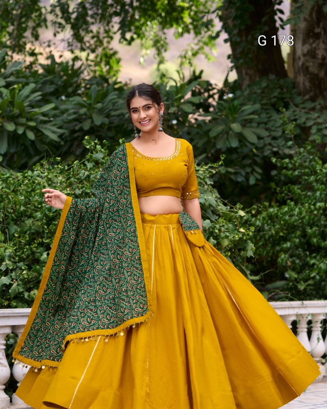 Woman in a yellow traditional outfit with a green dupatta standing outdoors.