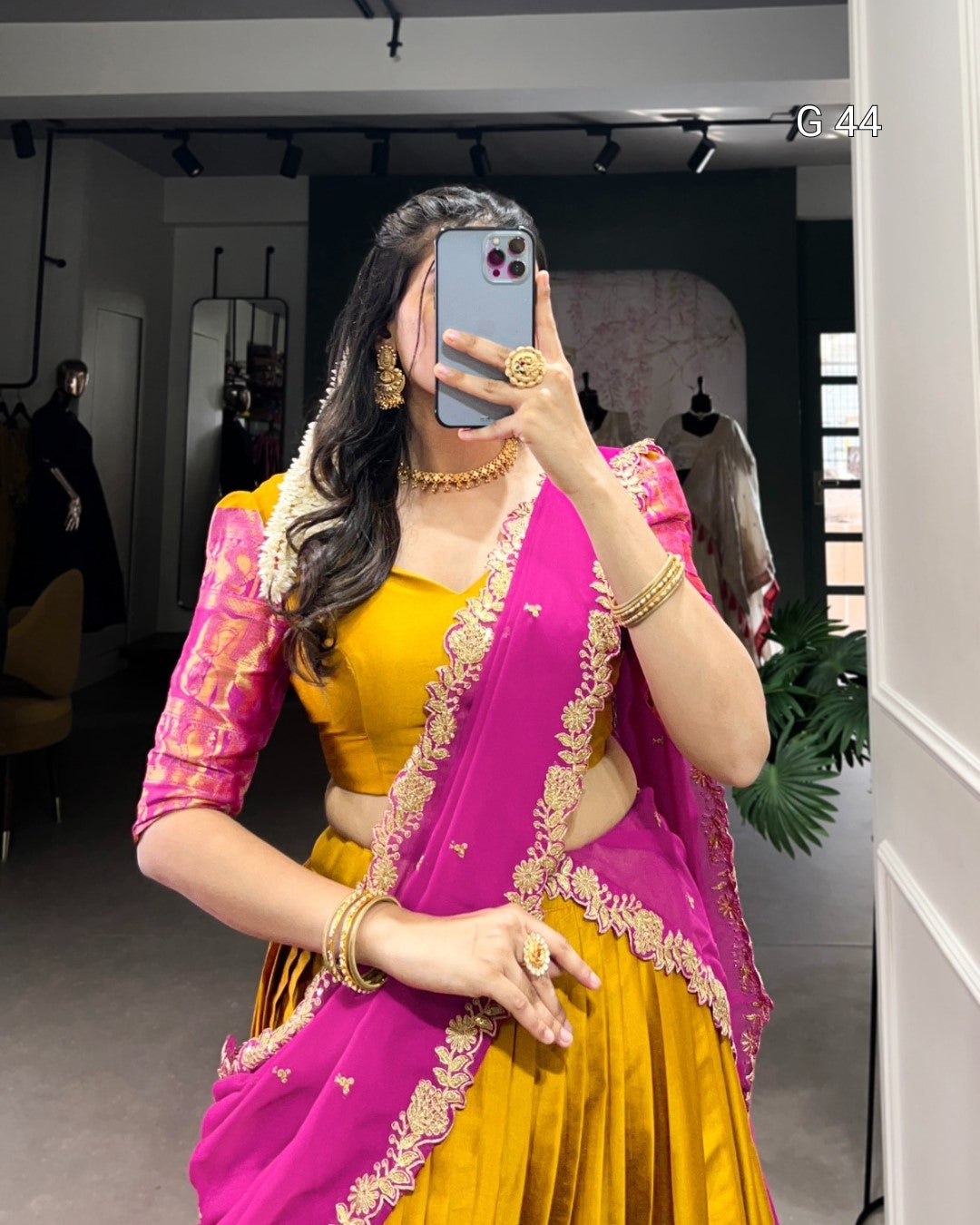 Woman wearing a yellow and pink saree with gold jewelry in a store setting.