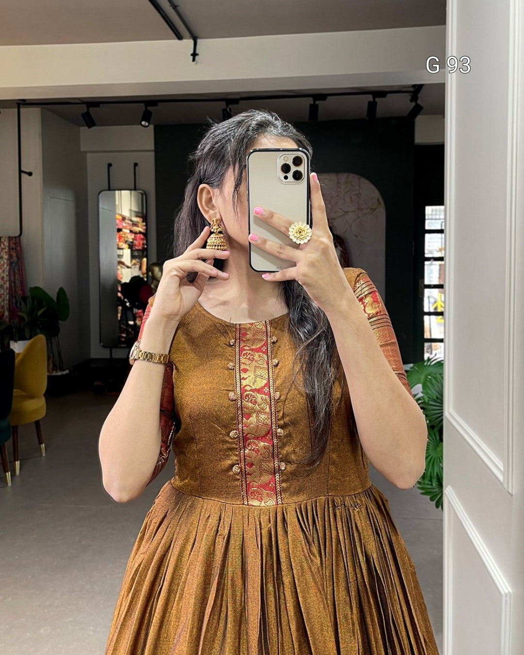 Woman taking a mirror selfie wearing an embroidered brown dress in a room.