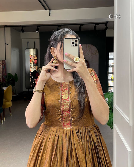 Woman taking a mirror selfie wearing an embroidered brown dress in a room.