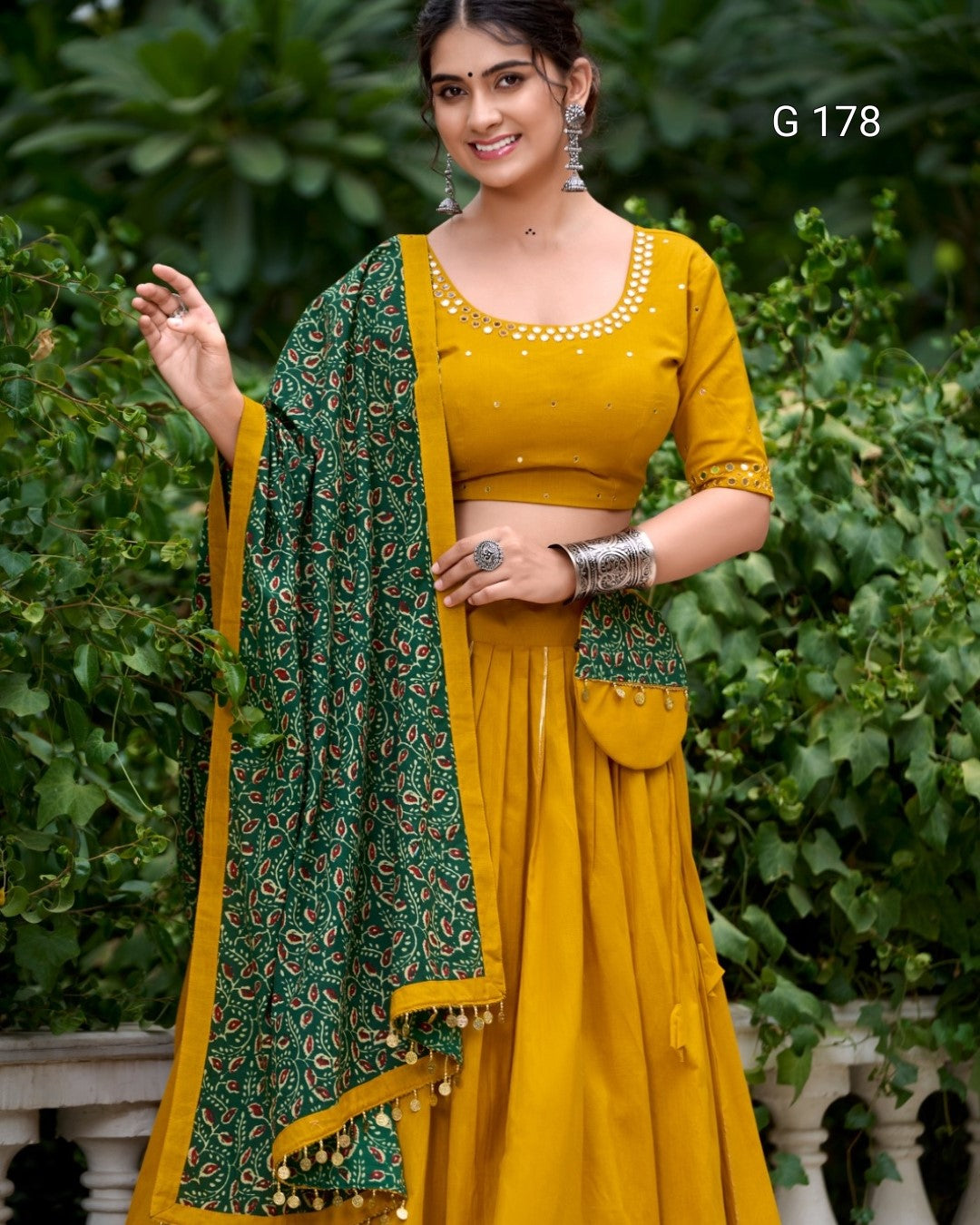 Woman wearing a yellow saree with green border against a green leafy background