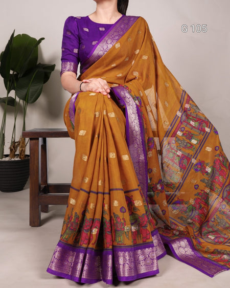 Woman wearing a mustard yellow and purple saree with a colorful pattern, standing against a neutral background.