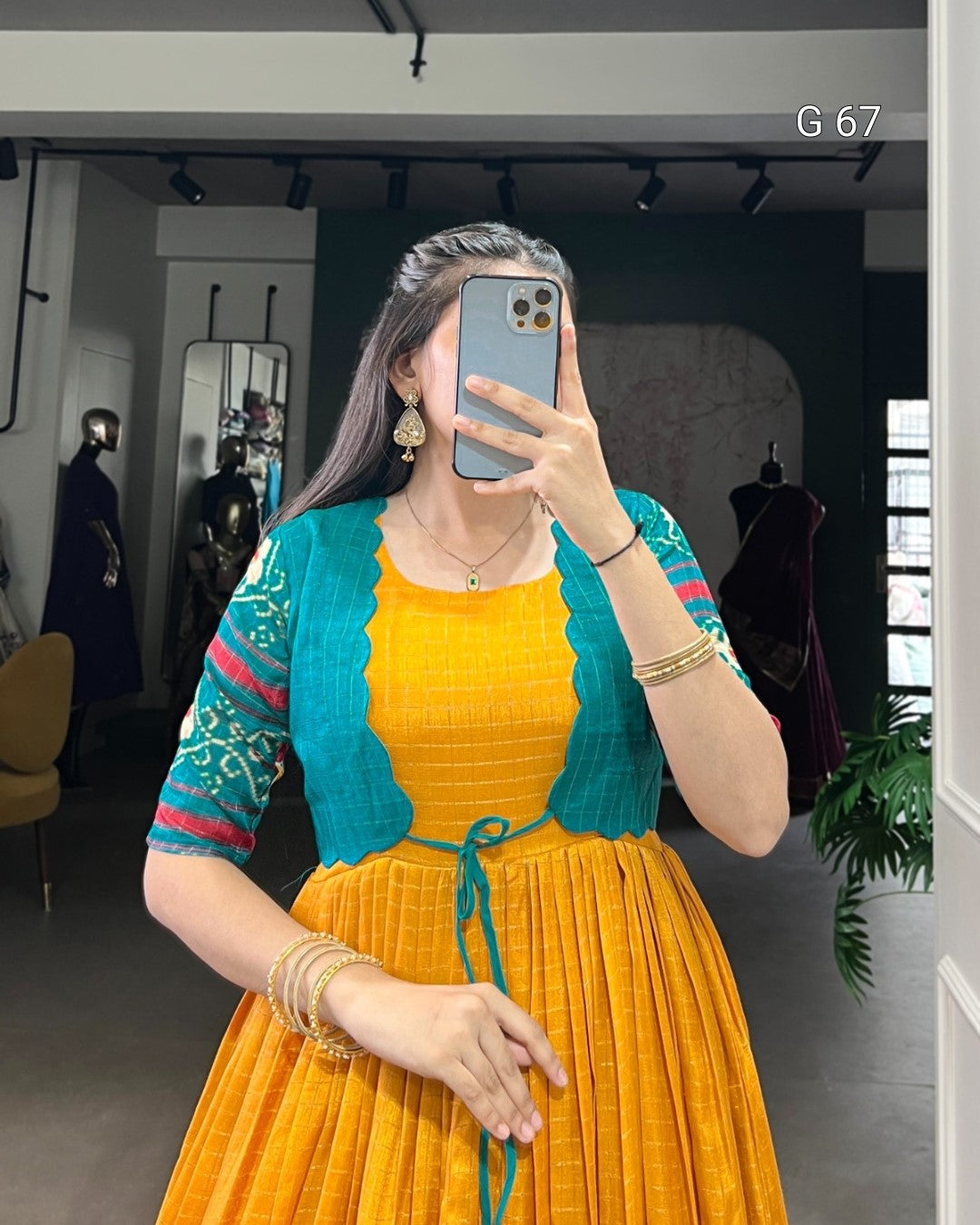 Woman taking a mirror selfie wearing a yellow dress with a blue cardigan in an indoor setting.