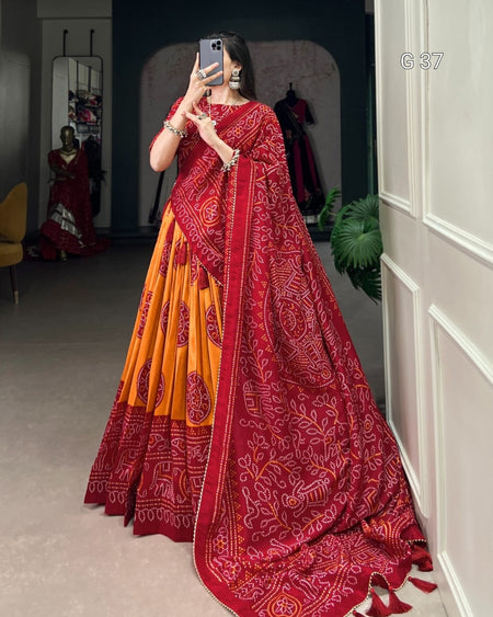 Person wearing a red and orange saree with a pattern, standing in a room.