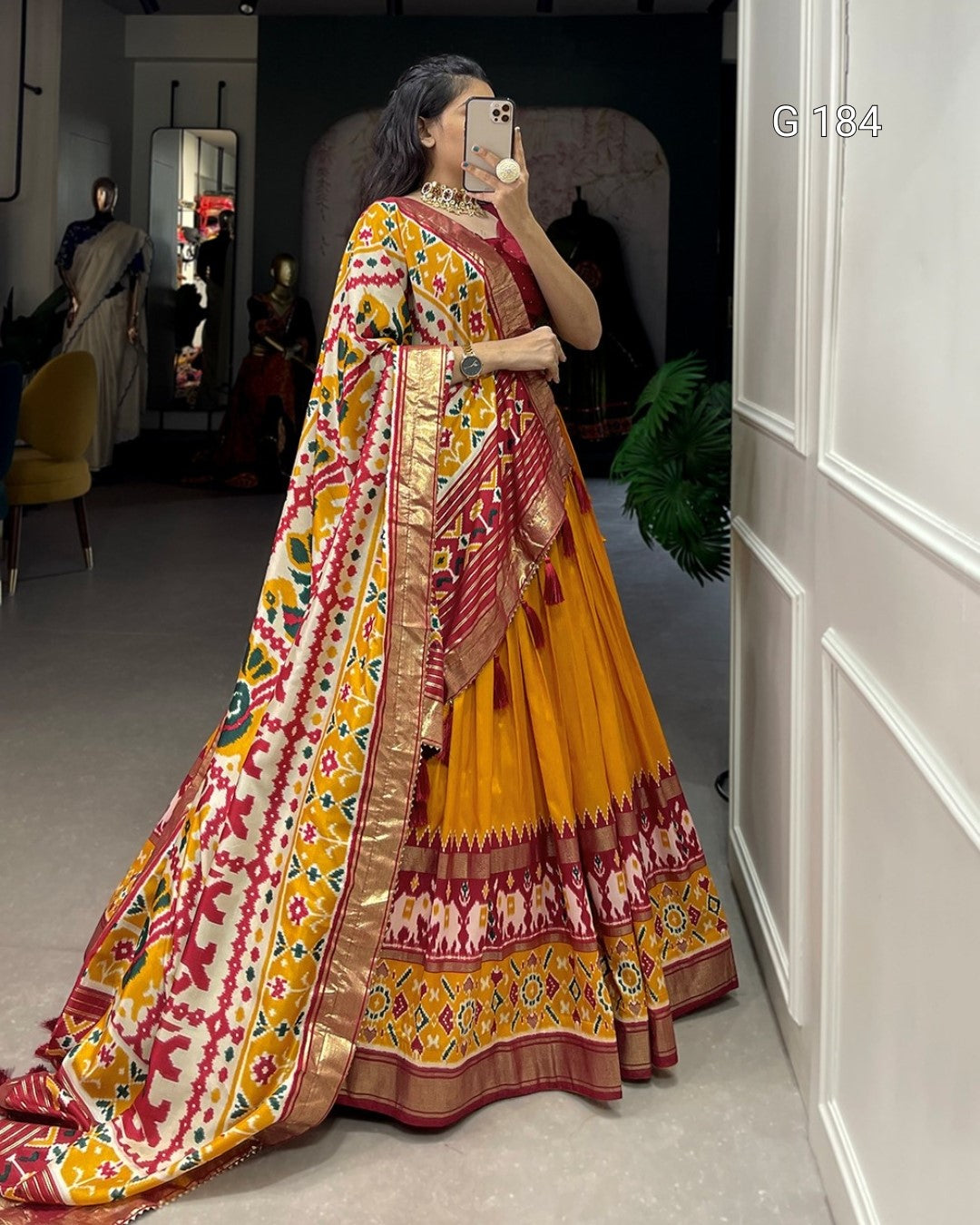 Woman wearing a colorful saree taking a mirror selfie in a room.