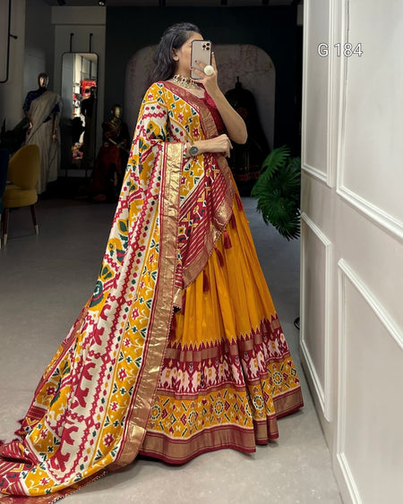 Woman wearing a colorful saree taking a mirror selfie in a room.