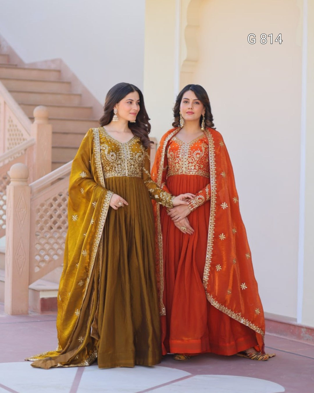 Two women in traditional embroidered dresses standing in front of a decorative staircase.