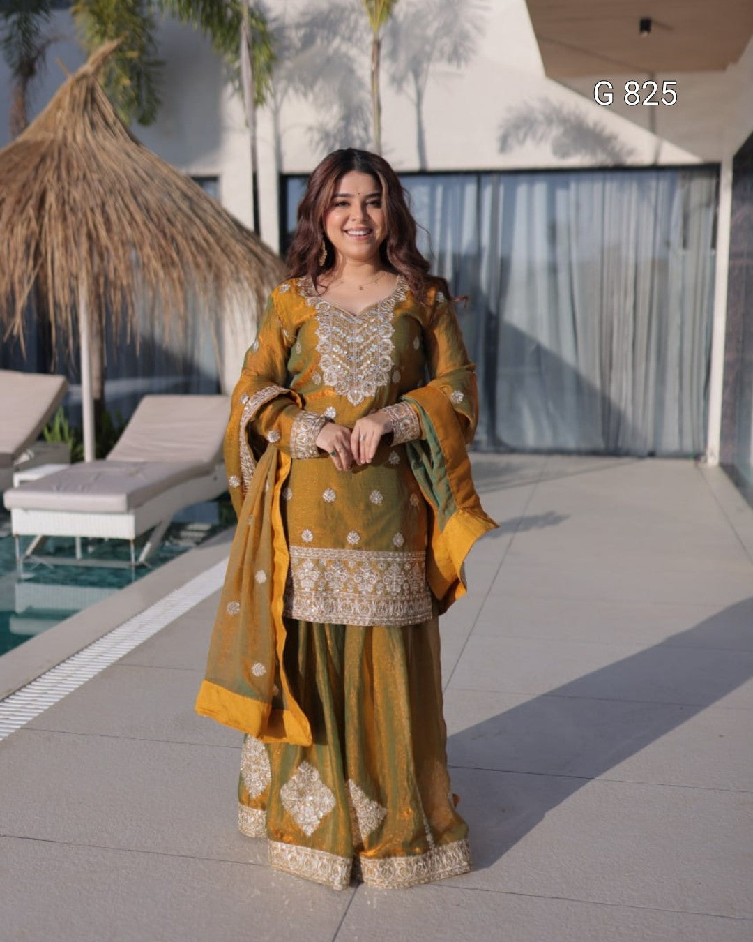 Woman in traditional mustard yellow and gold outfit standing by a poolside.