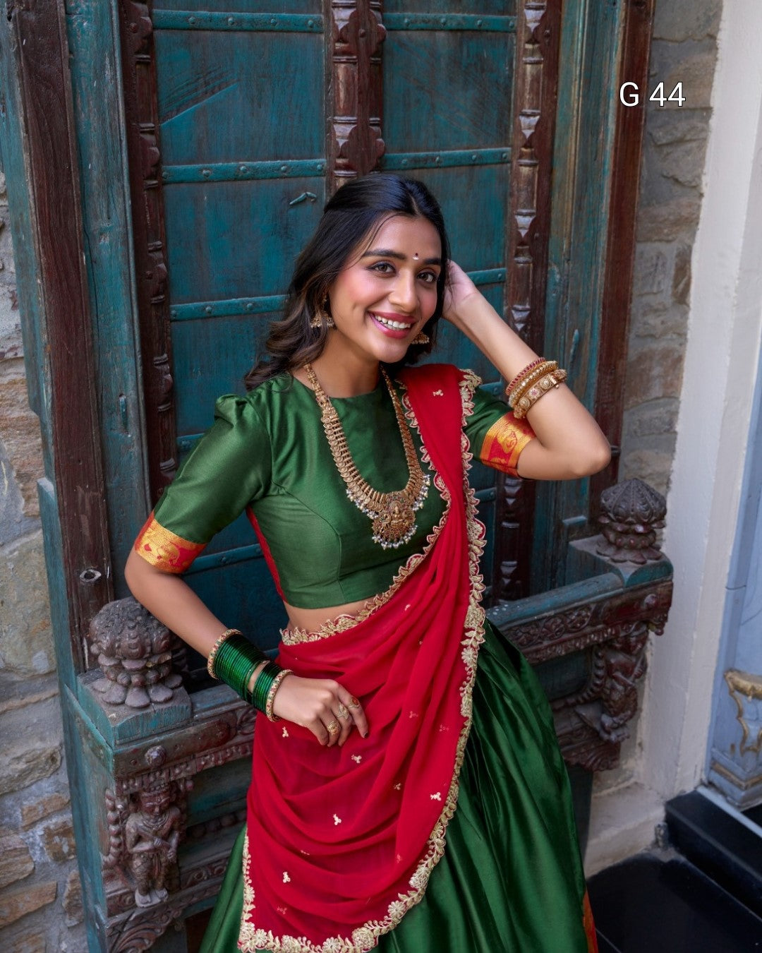 Woman in a green and red traditional outfit standing in front of an ornate door.