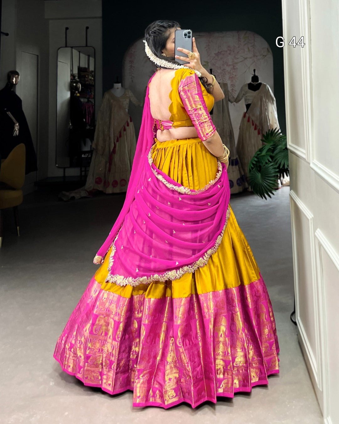Person wearing a vibrant pink and yellow traditional outfit in a room with mirrors and clothing.