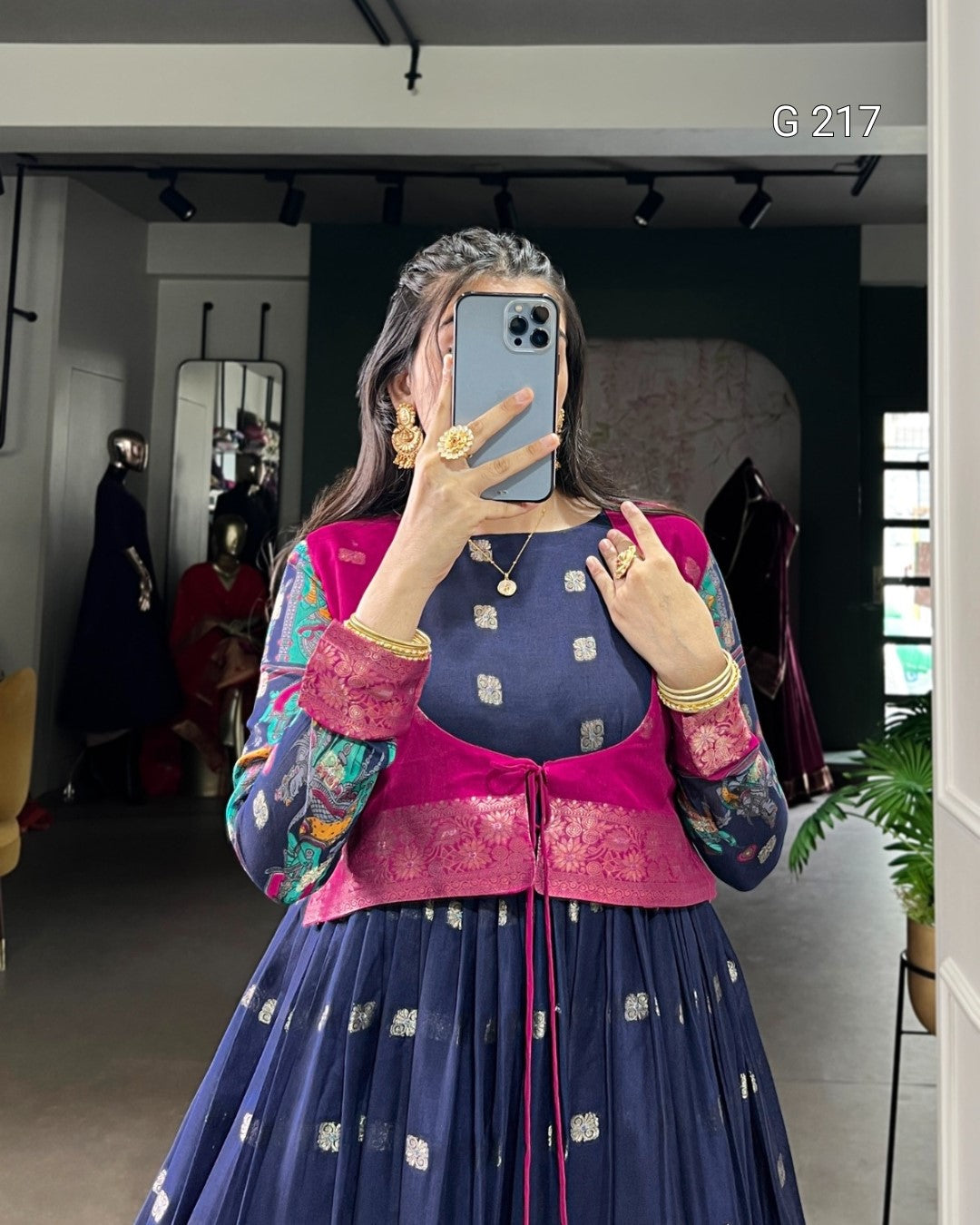 Person wearing a colorful traditional outfit with a blue and pink top and skirt, taking a mirror selfie.