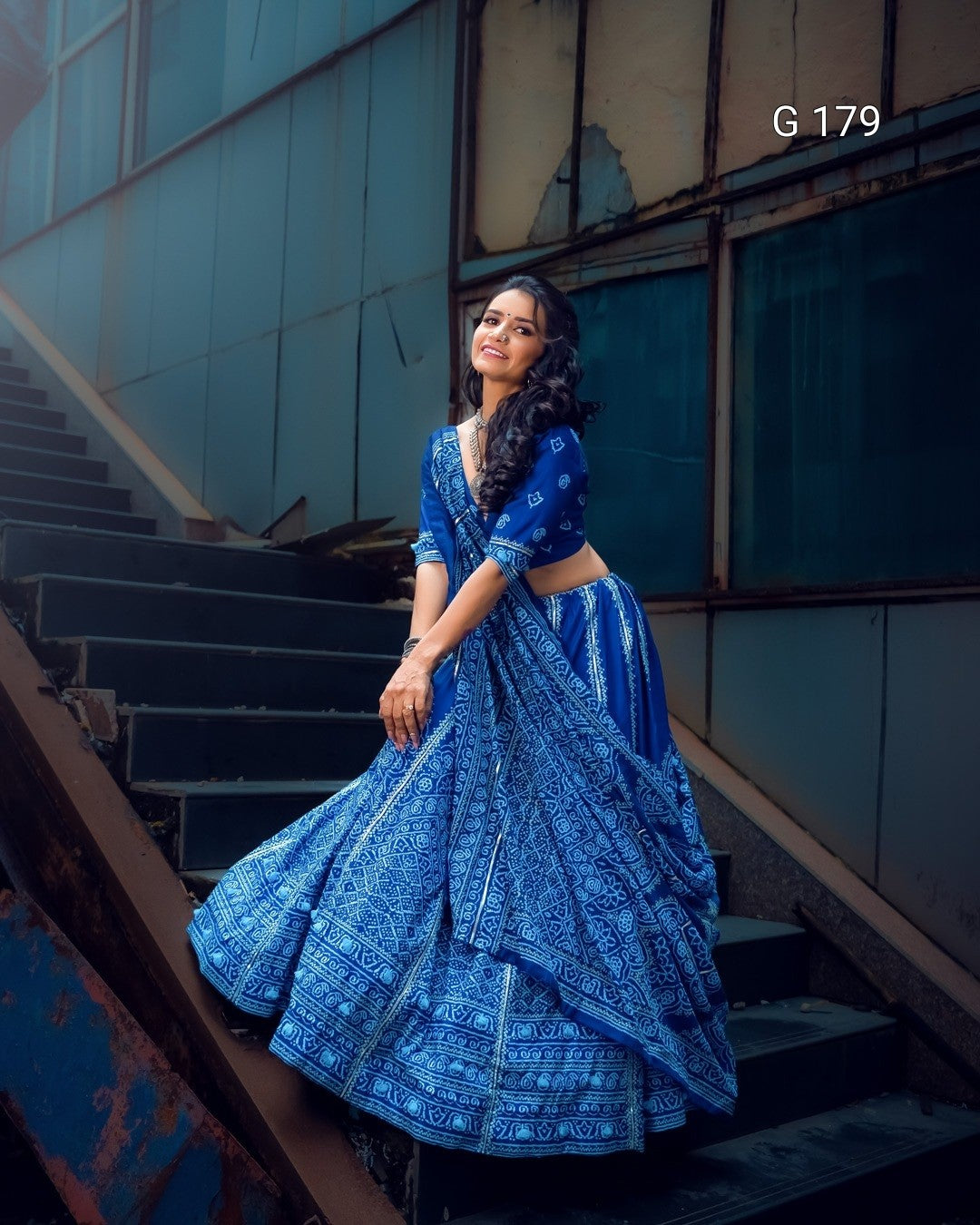 Woman in a blue traditional outfit standing on a staircase with a modern building background