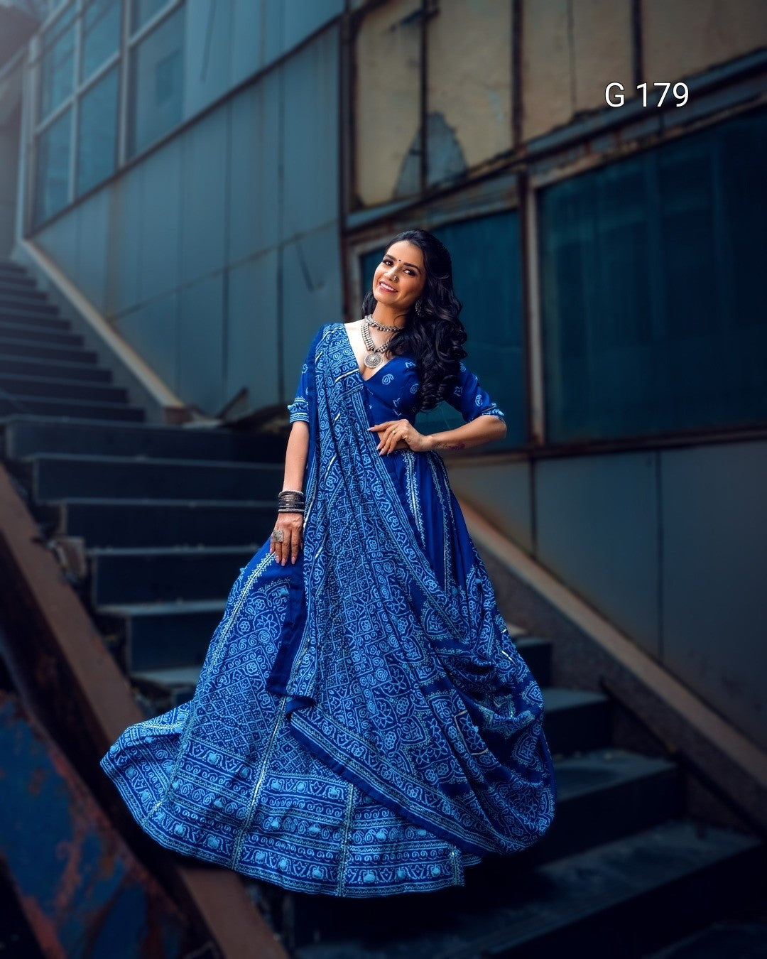 Woman in a blue traditional outfit standing on steps with a modern building in the background
