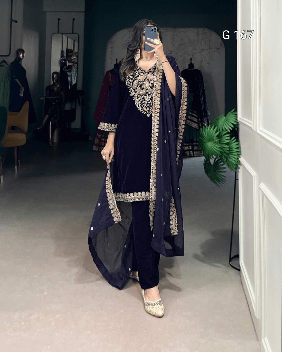 Person wearing a navy blue traditional outfit with intricate embroidery in a room.
