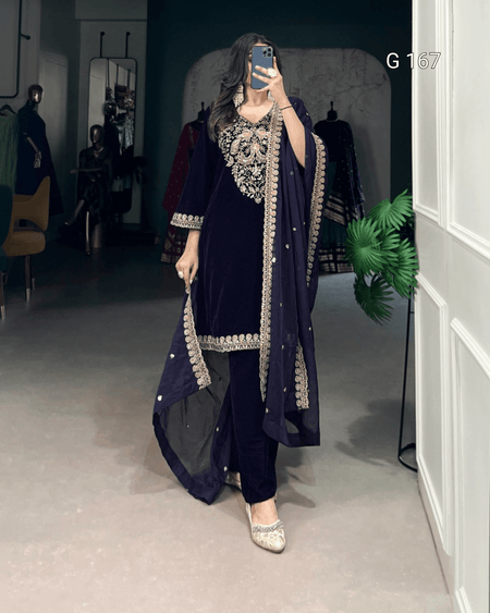 Person wearing a navy blue traditional outfit with intricate embroidery in a room.