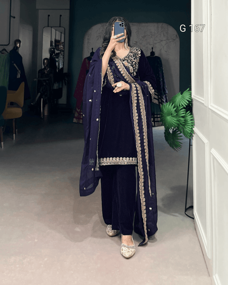 Person wearing a dark blue traditional outfit with intricate embroidery in a room.