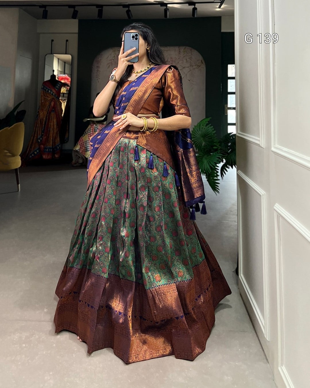 Person wearing a traditional outfit with a green and brown color scheme, standing in a room.