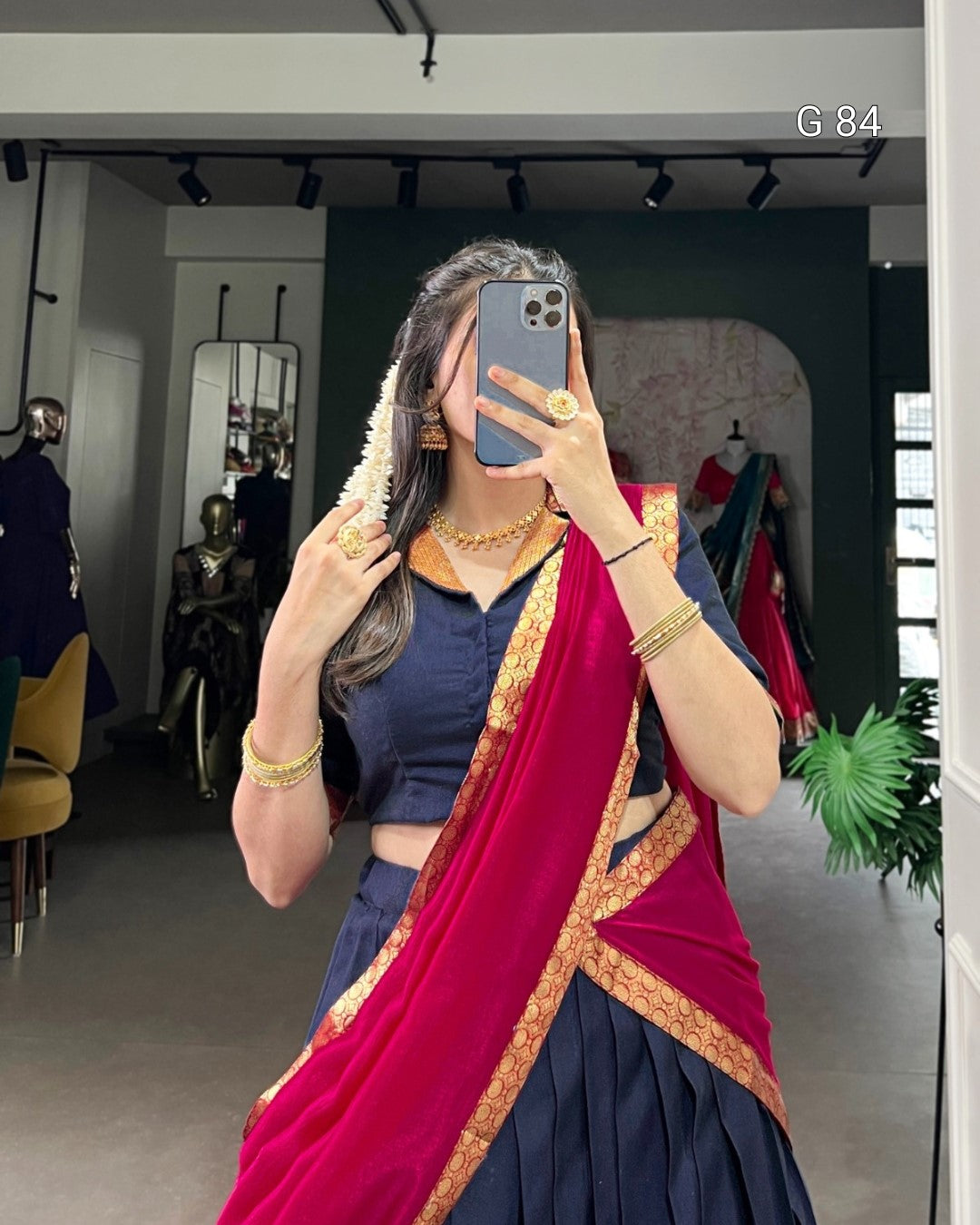 Woman taking a mirror selfie wearing a blue top and red saree with gold border.