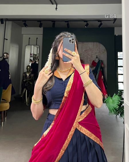 Woman taking a mirror selfie wearing a blue top and red saree with gold border.