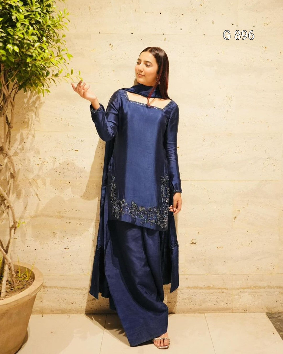 Woman wearing a blue traditional outfit standing against a textured wall.