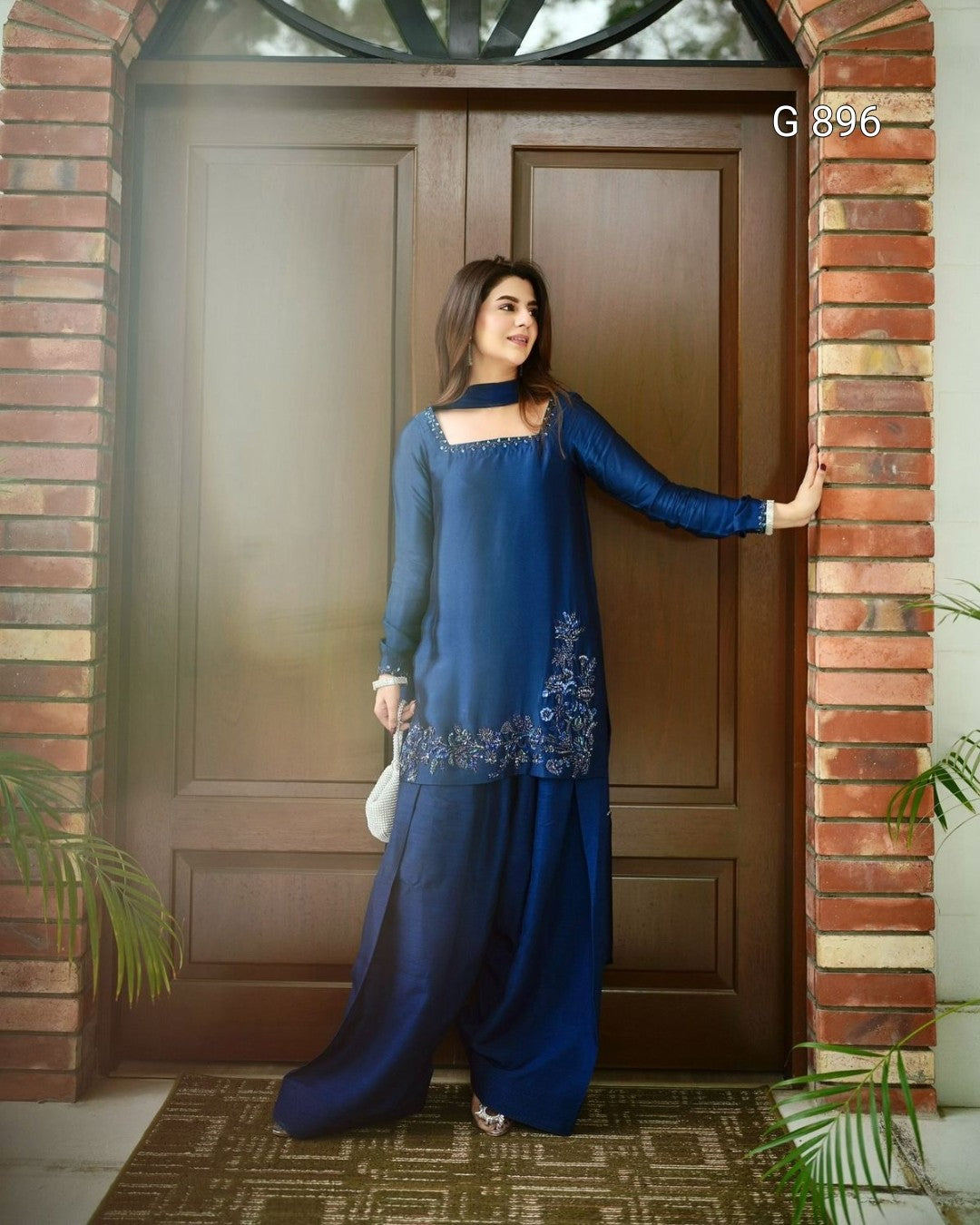 Woman in a blue traditional outfit standing in front of a wooden door.