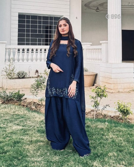Woman in a blue traditional outfit standing outdoors on grass.